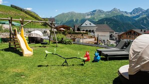 A playground with a slide and seesaw, surrounded by houses and mountains in the background. - Haus Sonnenterrasse (Fiss)