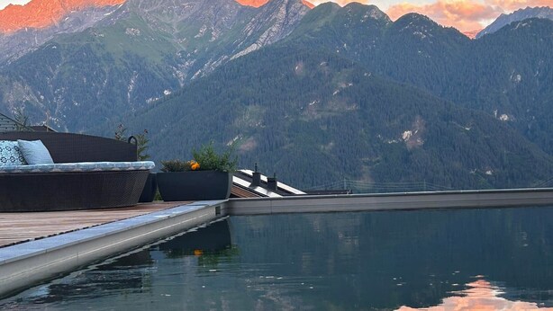 A pool with a wooden deck and a sofa with cushions. - Haus Sonnenterrasse (Fiss)