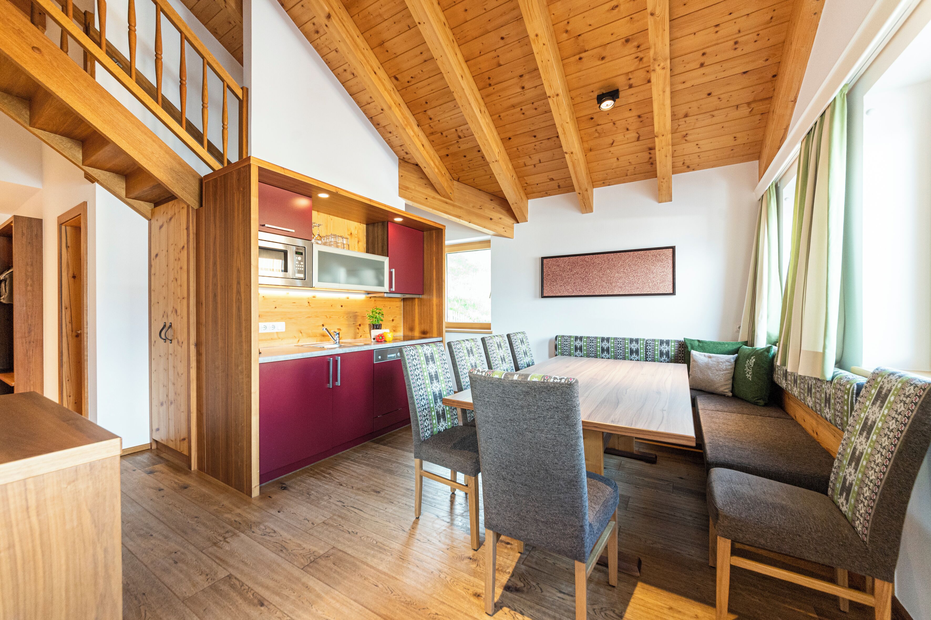 Una cocina moderna con vigas de madera, un comedor con mesa y sillas de madera, y un banco empotrado con cojines.