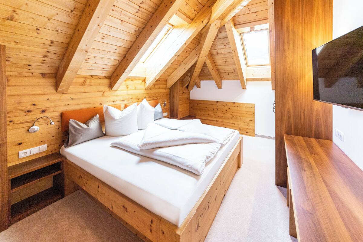 Quarto de madeira com uma cama, um banco e uma televisão.