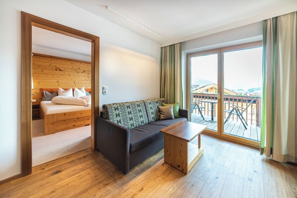 Una habitación moderna con suelo de madera, un sofá, una mesita y un balcón con vistas a un edificio.