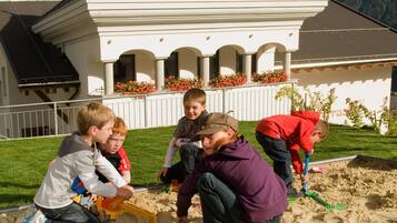 Children play on the sandy area surrounded by a building with a central entrance and balcony.