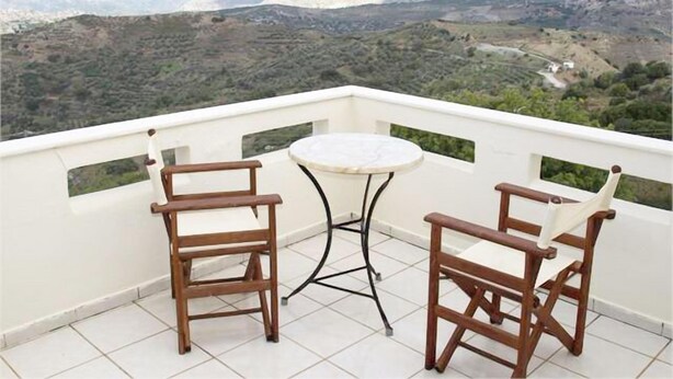 A balcony with two wooden chairs and a small round table, overlooking a mountainous landscape. - Aristea Hotel (Anogia)