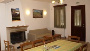 A dining room with a table set for four, a fireplace, and two wall-mounted paintings. - Aristea Hotel (Anogia)