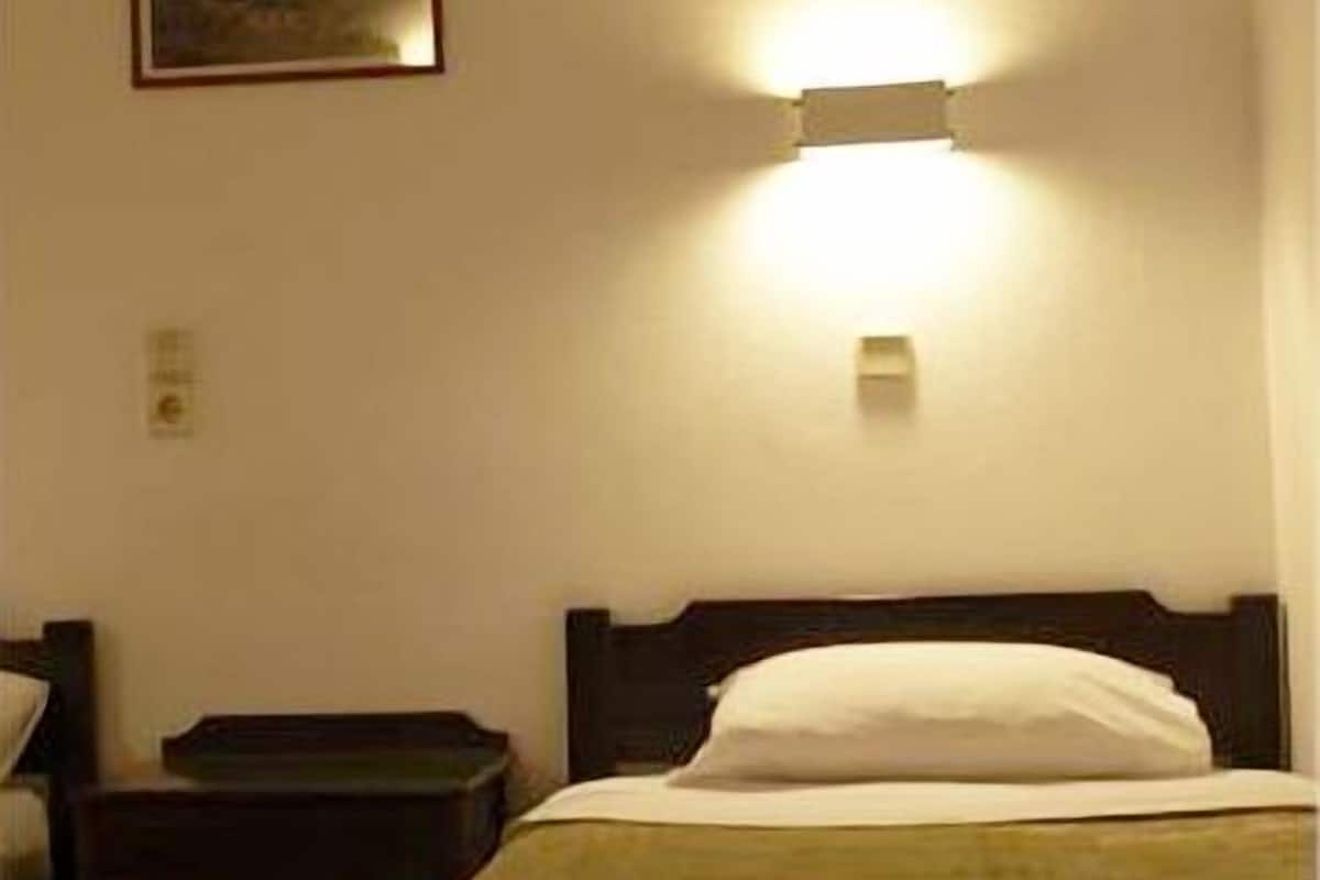 A hotel room with a bed, a nightstand, a wall-mounted light, and a framed picture on the wall.