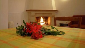 A dining area with a table set for two, a fireplace in the background, and a chair to the right. - Aristea Hotel (Anogia)