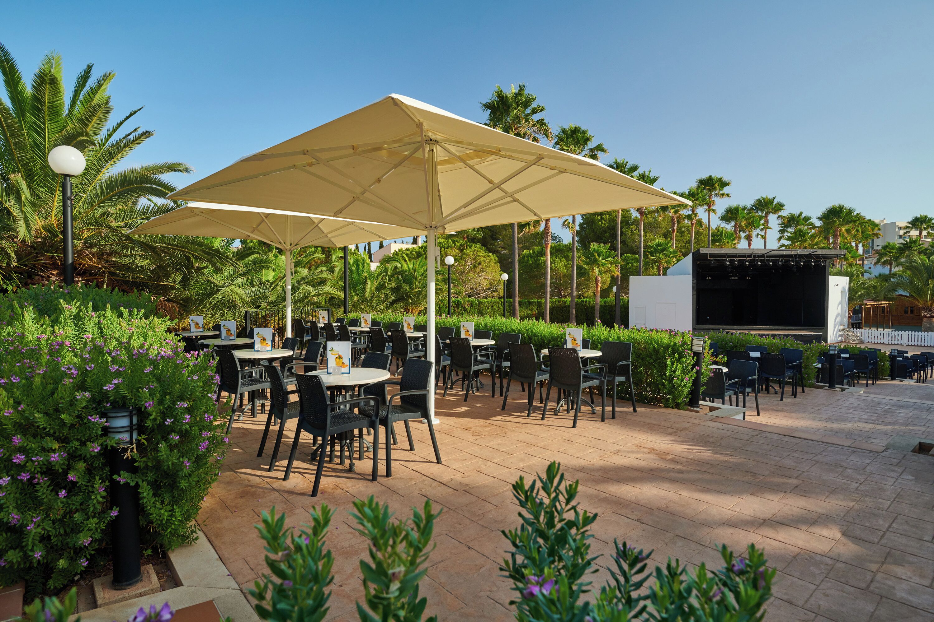 An outdoor patio with tables and chairs, a stage, and palm trees.