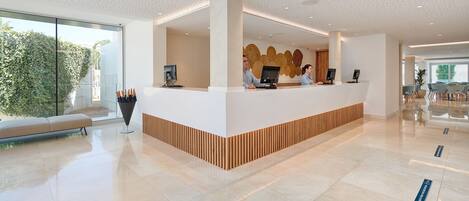 A modern reception desk with two monitors, a large window, and a seating area with a bench.