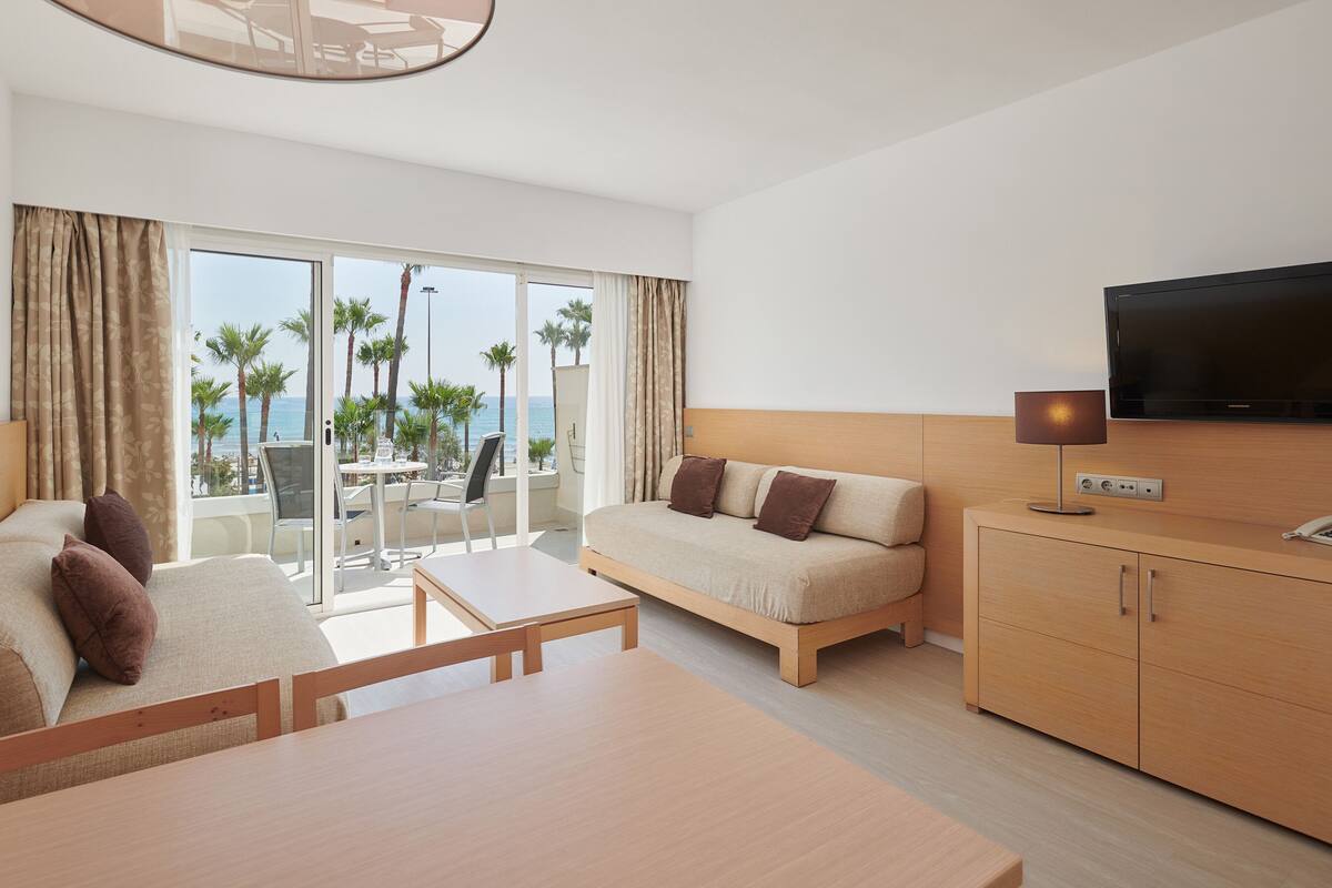 A modern hotel room with a balcony, a sofa, a TV, and a wooden cabinet.