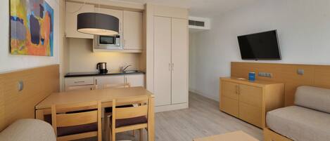 Una habitación de hotel moderna con kitchenette, comedor, sofá y televisor montado en la pared.