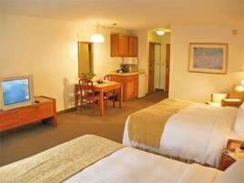 Habitación de hotel con dos camas, un escritorio con silla, un televisor y una kitchenette.