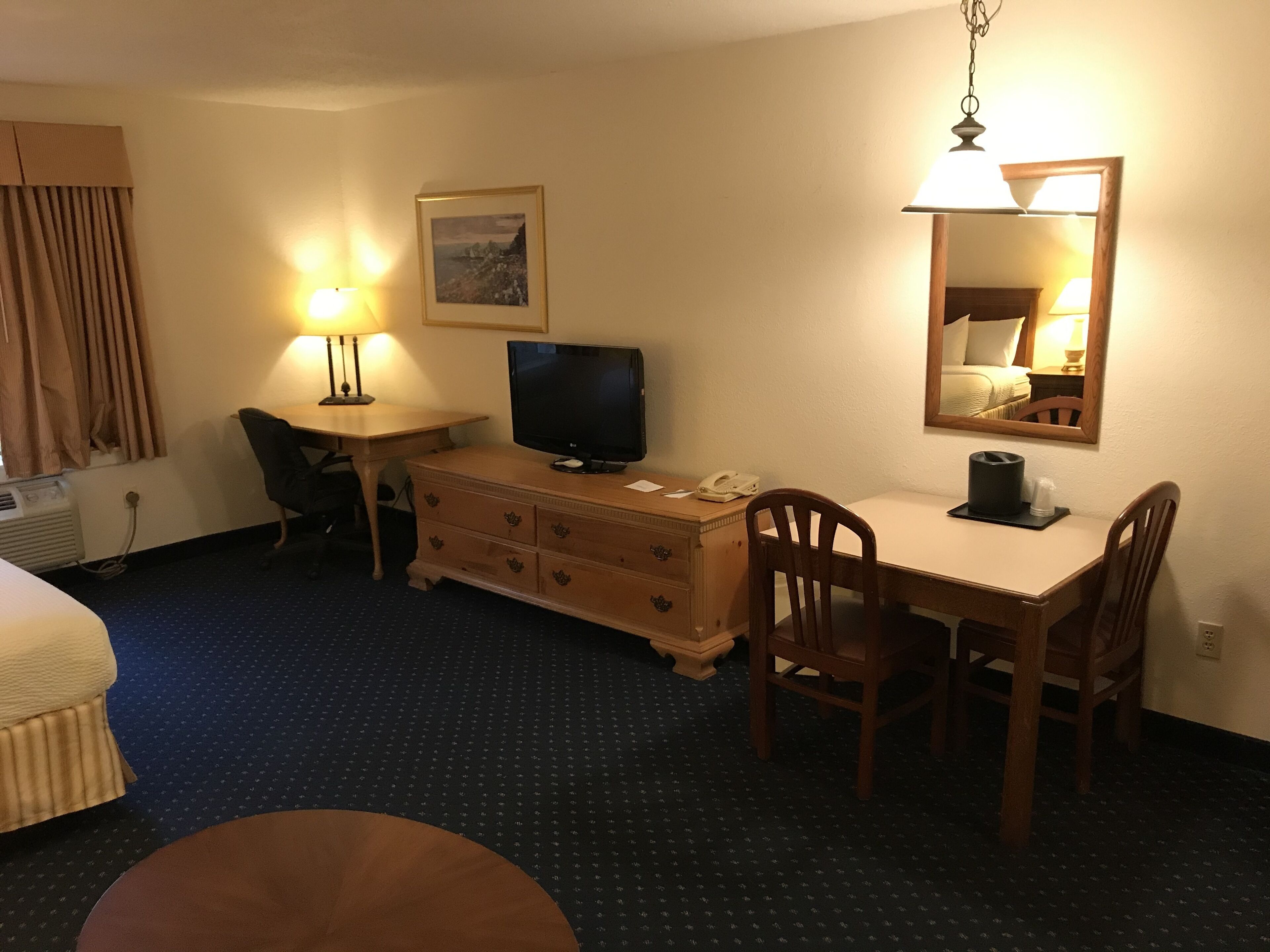 A hotel room with a bed, a desk with a computer, a TV, a chair, a dresser, and a mirror.