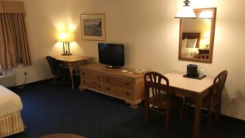 A hotel room with a bed, a desk with a computer, a TV, a chair, a dresser, and a mirror.