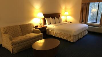 Una habitación de hotel con cama, sofá, mesita de noche y una mesa de centro redonda.