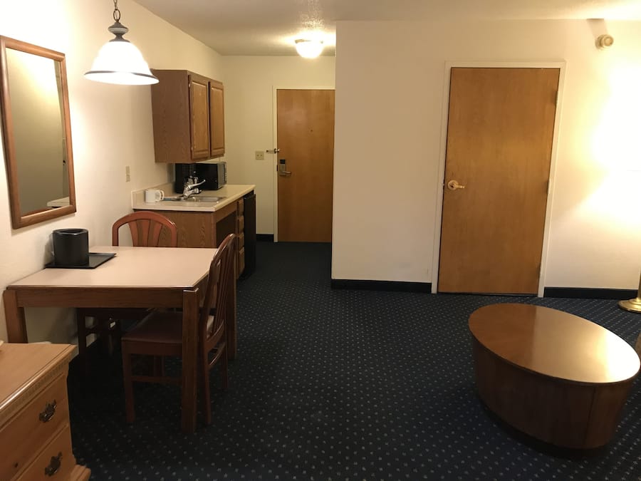 A compact hotel room with a dining area, kitchenette, and a large wooden door.