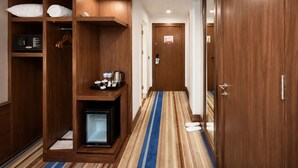 Ett hotellrum med en garderob i trä, en minibar, ett litet kylskåp och en randig matta.