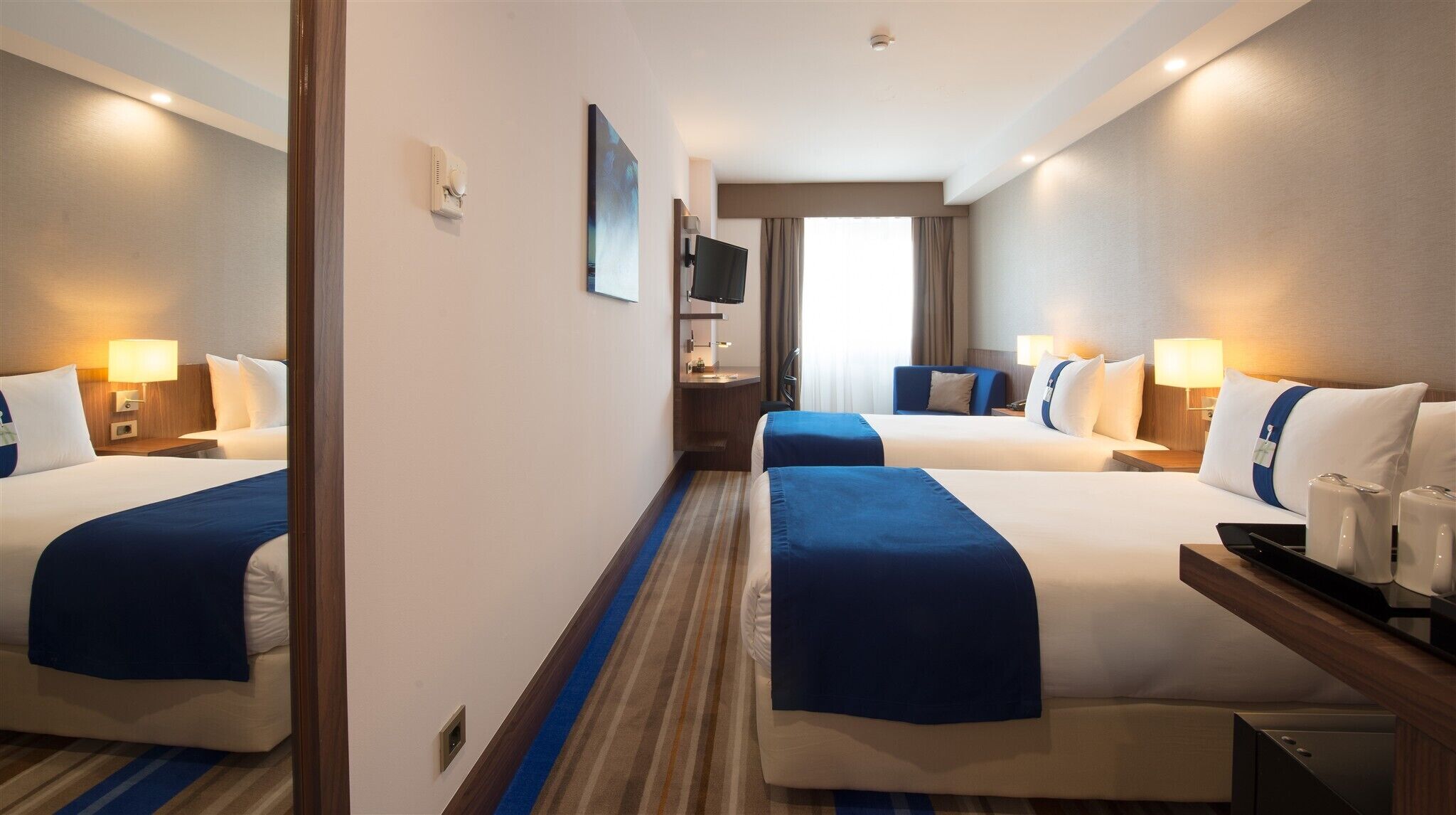 A hotel room with two beds, a TV, a desk, and a window.
