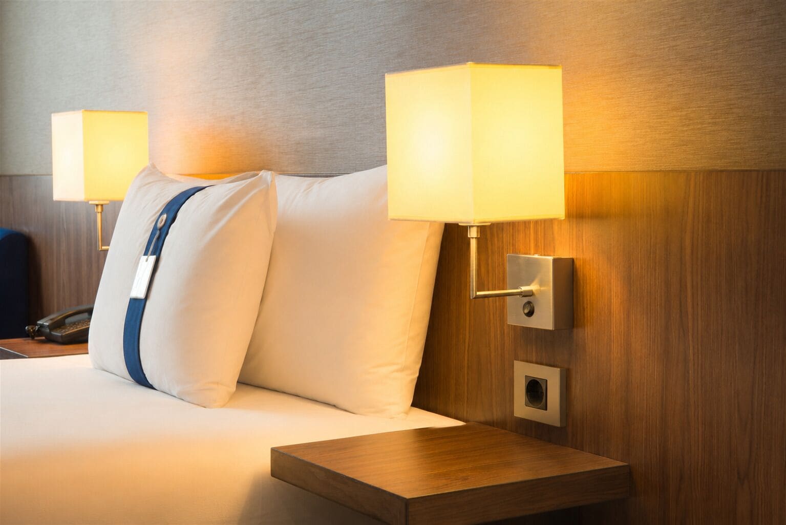 A hotel room with a bed, two bedside lamps, a bedside table, and a phone on the nightstand.