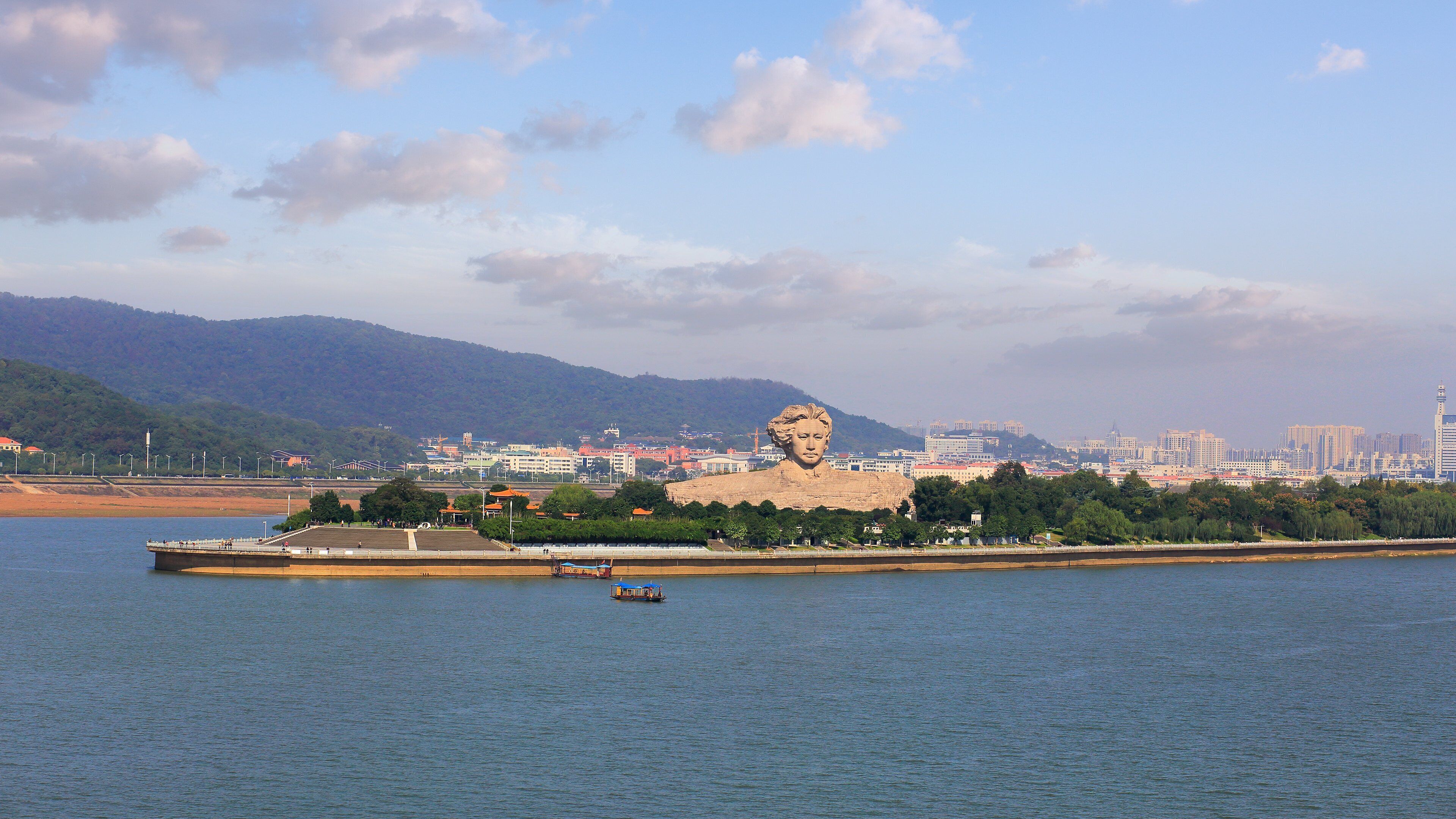 A large statue on an island with a cityscape in the background.