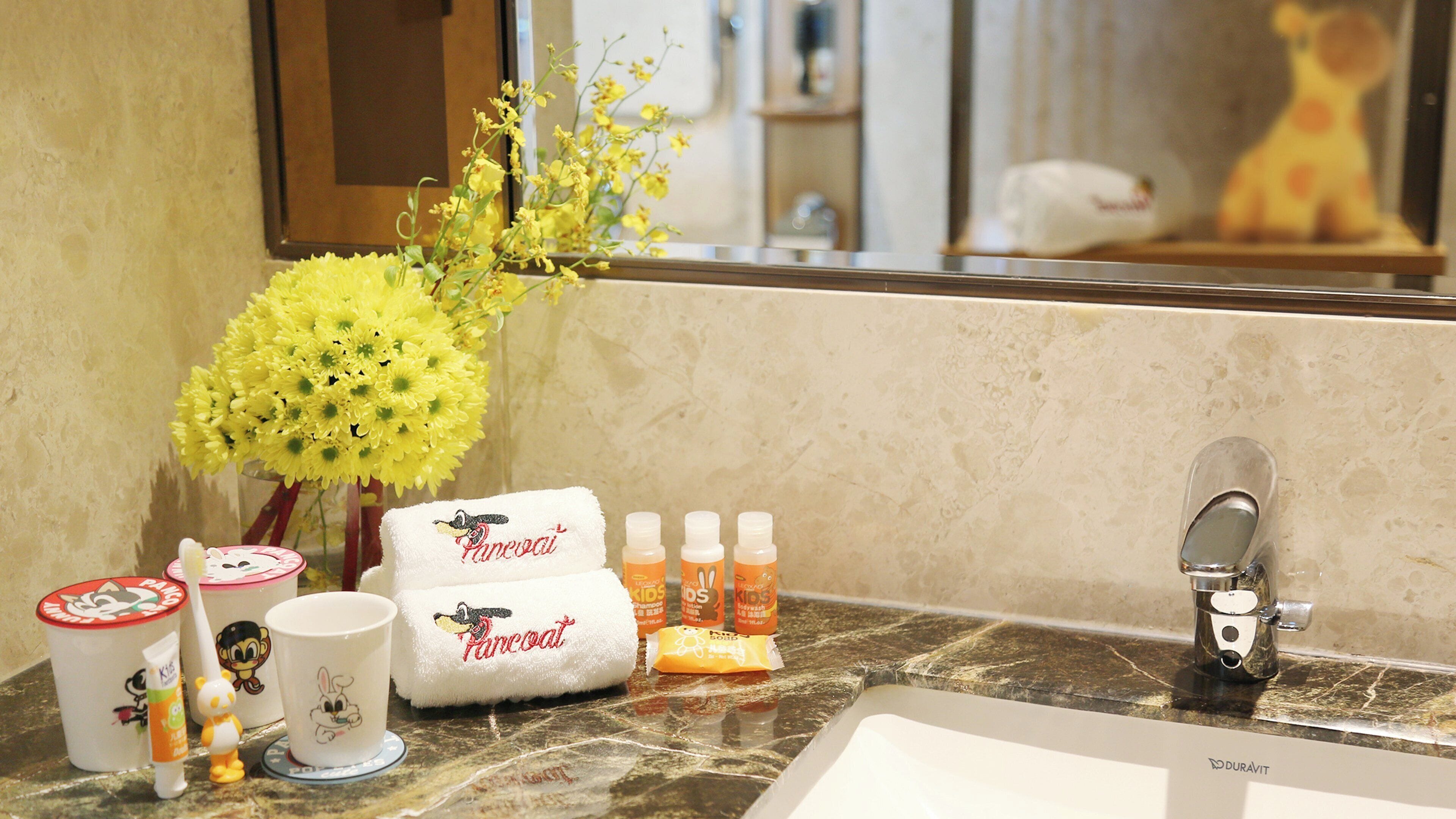 A bathroom vanity with a mirror, a sink, toiletries, and a decorative yellow flower arrangement.