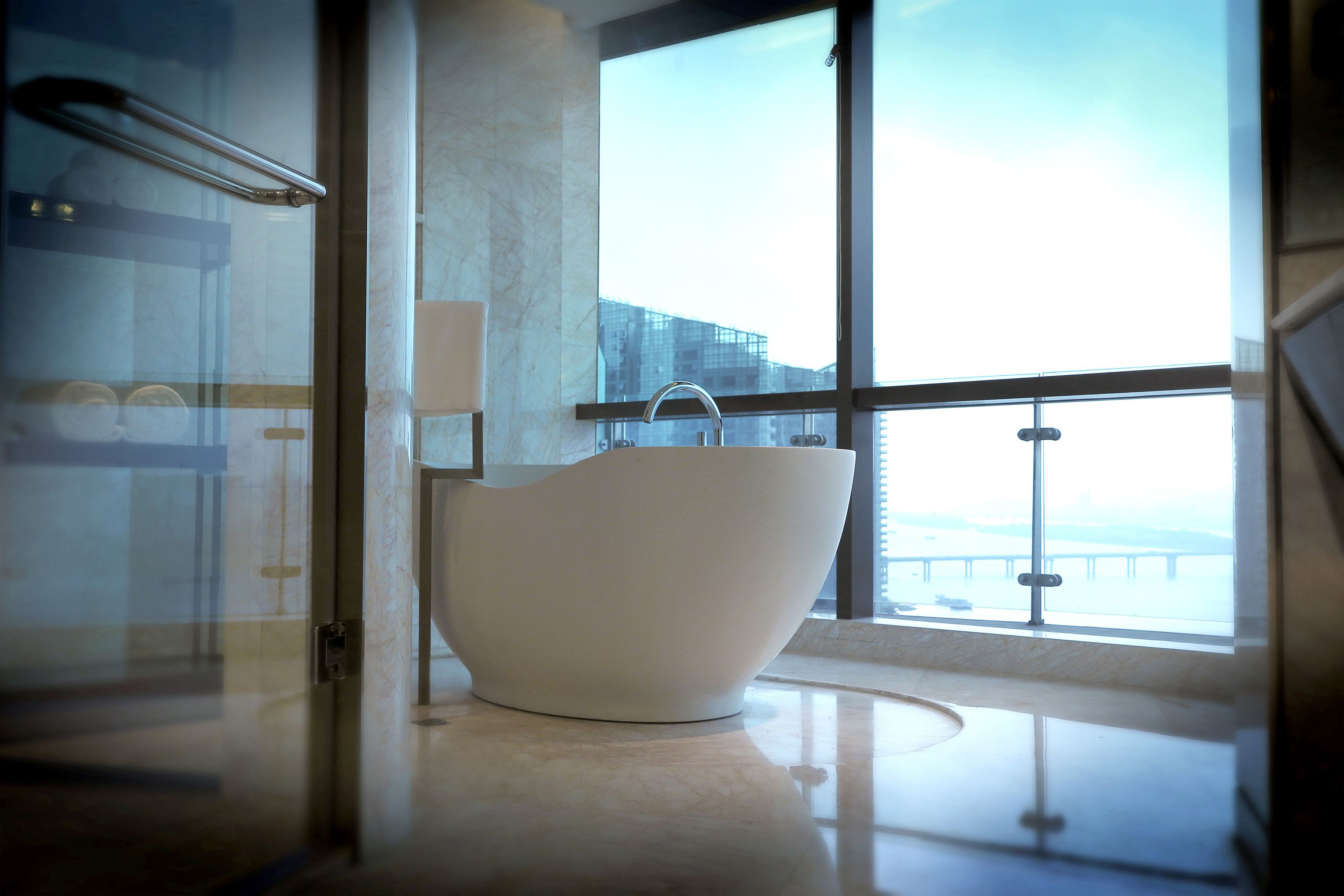 Une salle de bain moderne avec une baignoire sur pieds, une douche en verre et une vue sur un pont, visible à travers de grandes fenêtres.