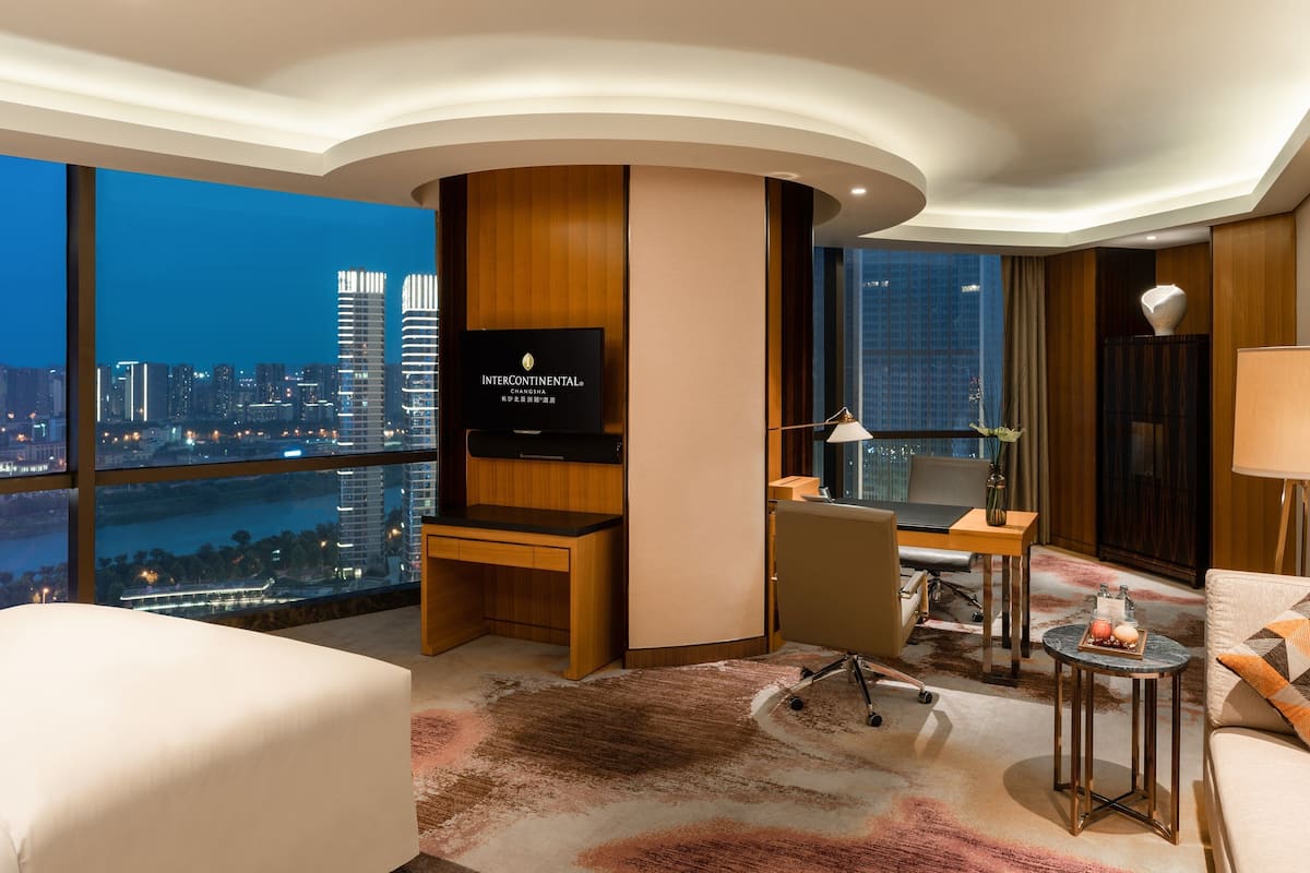 A modern hotel room with a city view, a desk, a sofa, and a TV.