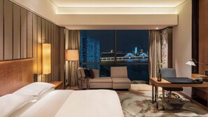A hotel room with a bed, a desk, a chair, a sofa, and a view of a cityscape at night. - InterContinental Changsha by IHG (Changsha)