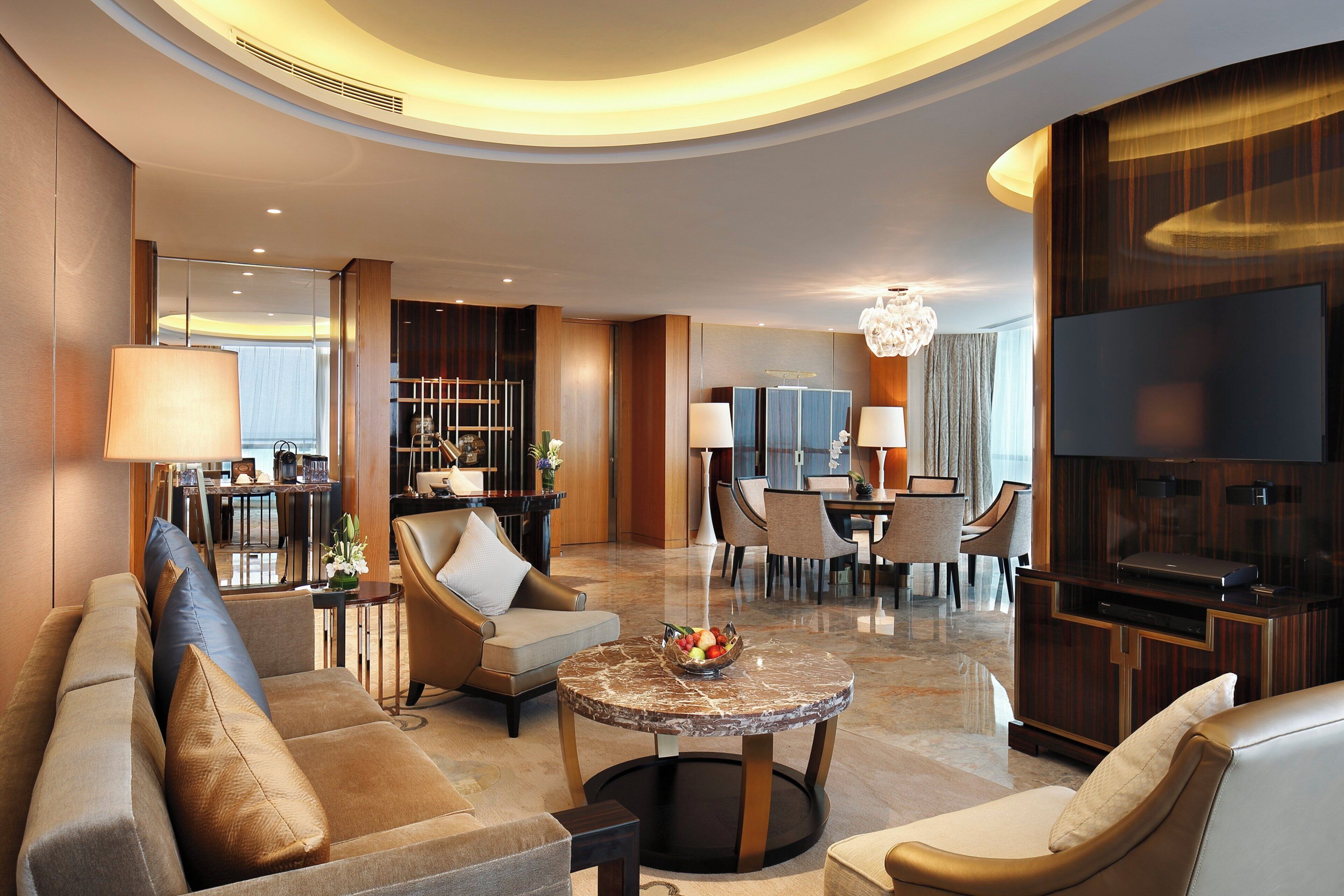 A modern hotel lobby with a seating area, a dining space, and a TV.
