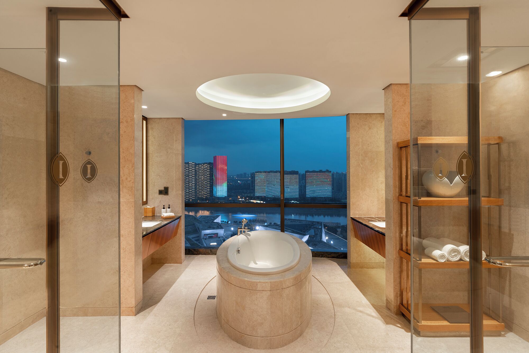 A modern bathroom with a large bathtub, a glass shower enclosure, and a city view.