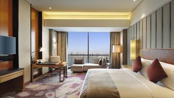 Ein Hotelzimmer mit einem Bett, einem Schreibtisch, einem Sessel sowie einem Fernseher und Blick auf die Stadt.