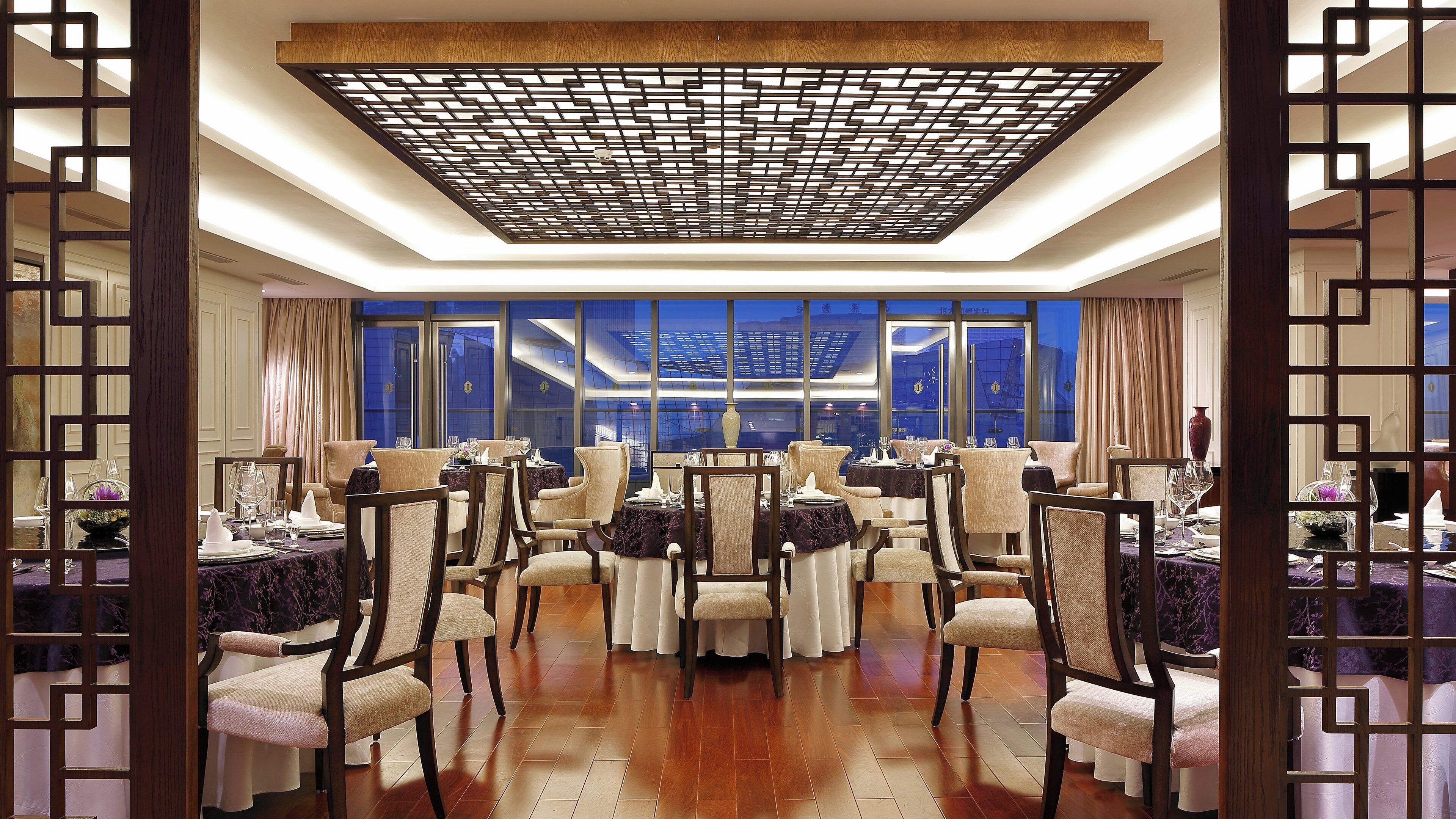 Un espace repas avec des tables dressées pour le service, un plafond décoratif et de grandes fenêtres offrant une vue agréable.