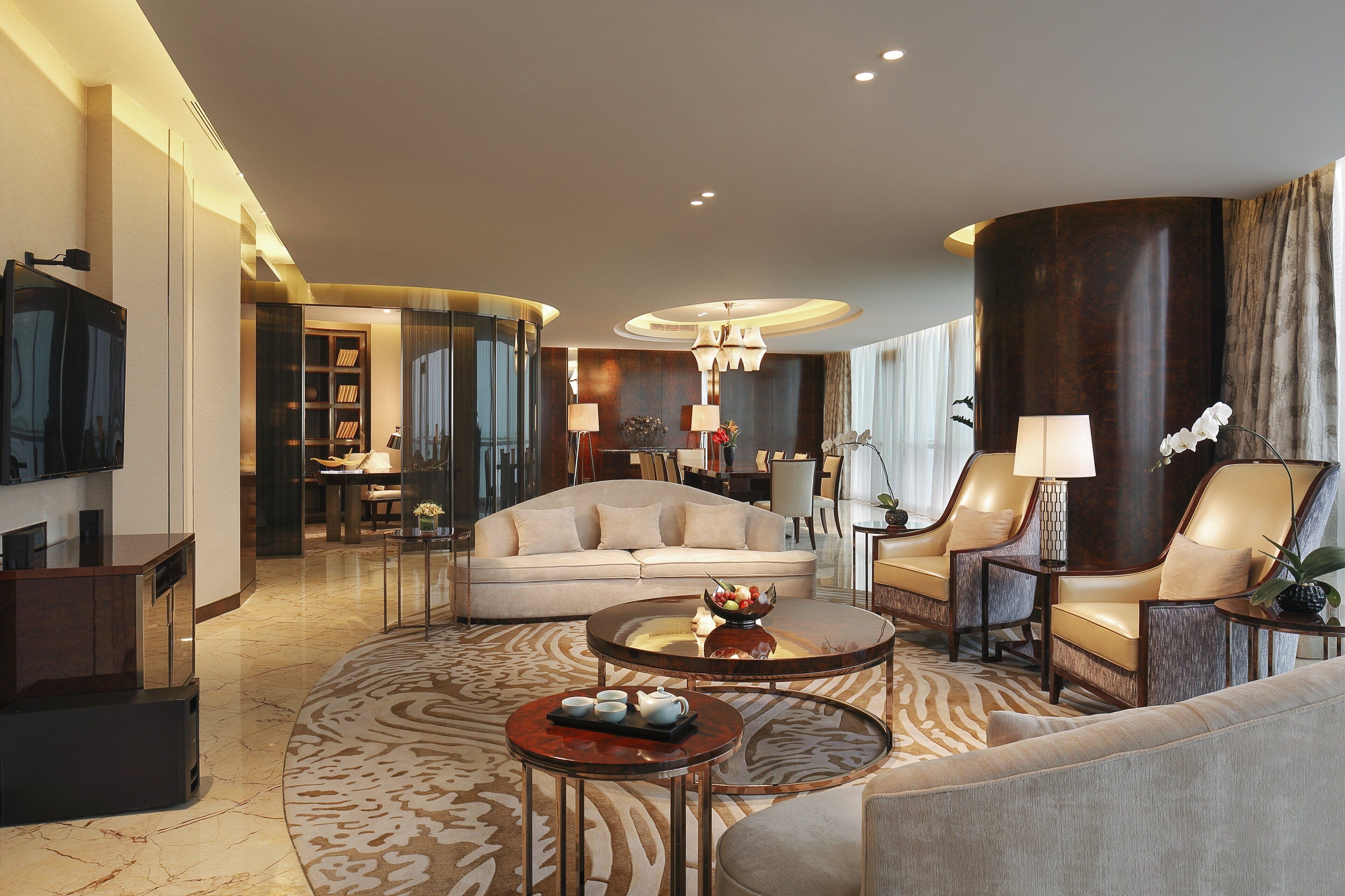 A modern living room with a sofa, armchairs, a coffee table, and a TV.