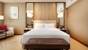 A hotel room with a large bed, a bedside table, a nightstand, a red pillow, a white wall, and a framed picture. - Luxury Blue Horizon Hotel (Hot Spring Hotel) (Dongying)