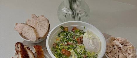 A meal with sliced meat, a salad, and a bowl of soup, accompanied by flowers in a vase.