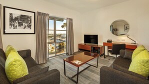 A modern hotel room with a large window, a flat-screen TV, a desk, and a comfortable seating area with two sofas. - Quest Melbourne Airport (Melbourne Airport)