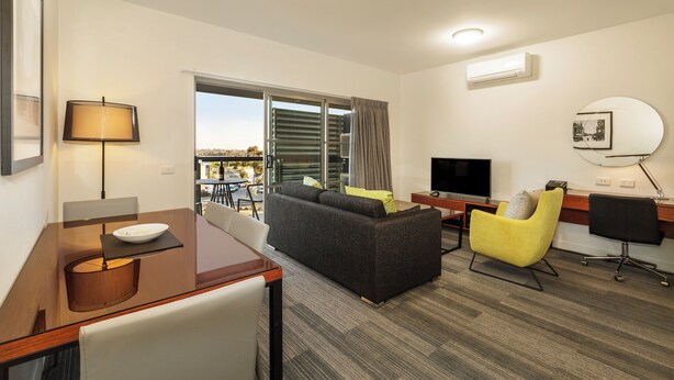 A modern hotel room with a sofa, a dining table, a TV, and a desk. - Quest Melbourne Airport (Melbourne Airport)