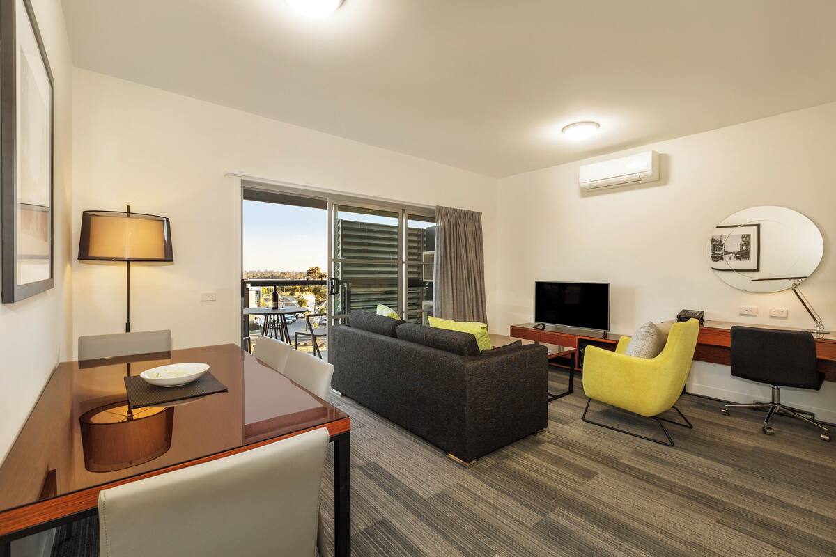 Ein modernes Hotelzimmer mit Sofa, Esstisch, Fernseher und Schreibtisch.