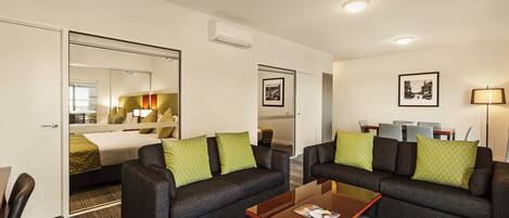 A hotel room with a bed, two sofas, a coffee table, and a dining area with chairs and a table.