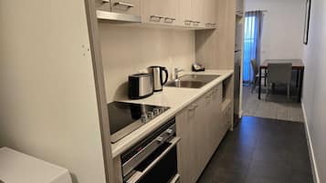 Et moderne køkken med indbygget ovn, komfur og vask. Spiseområde med bord og stole ses i baggrunden.