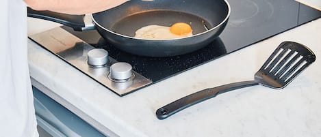 A person cooking an egg in a pan on a stove.