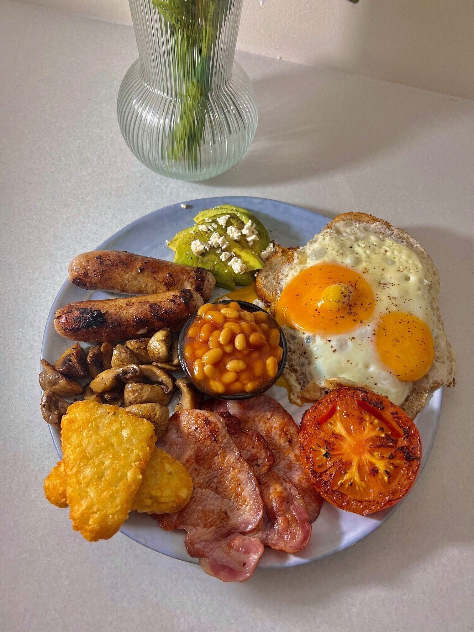 Une assiette de nourriture pour le petit-déjeuner comprenant des œufs, des saucisses, des haricots, des champignons, du bacon et une tomate.