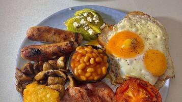 Une assiette de nourriture pour le petit-déjeuner comprenant des œufs, des saucisses, des haricots, des champignons, du bacon et une tomate.