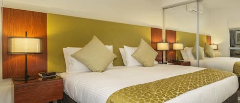 Una habitación de hotel con una cama grande, una mesita de noche, una lámpara, un espejo y un equipo de aire acondicionado.