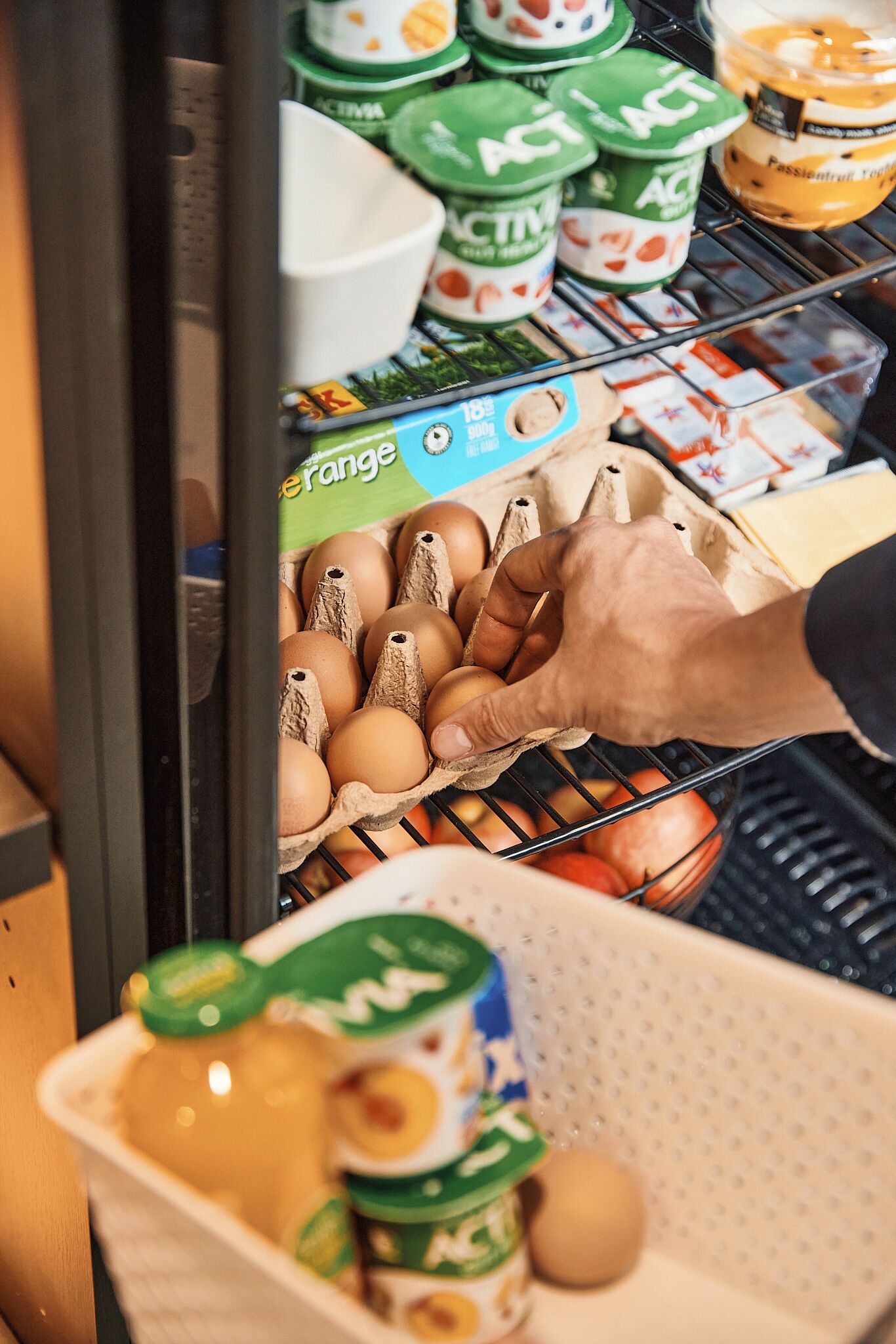 A hand selecting eggs from a carton in a refrigerated section of a grocery store.