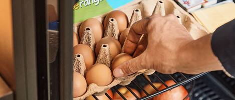 A hand selecting eggs from a carton in a refrigerated section of a grocery store.