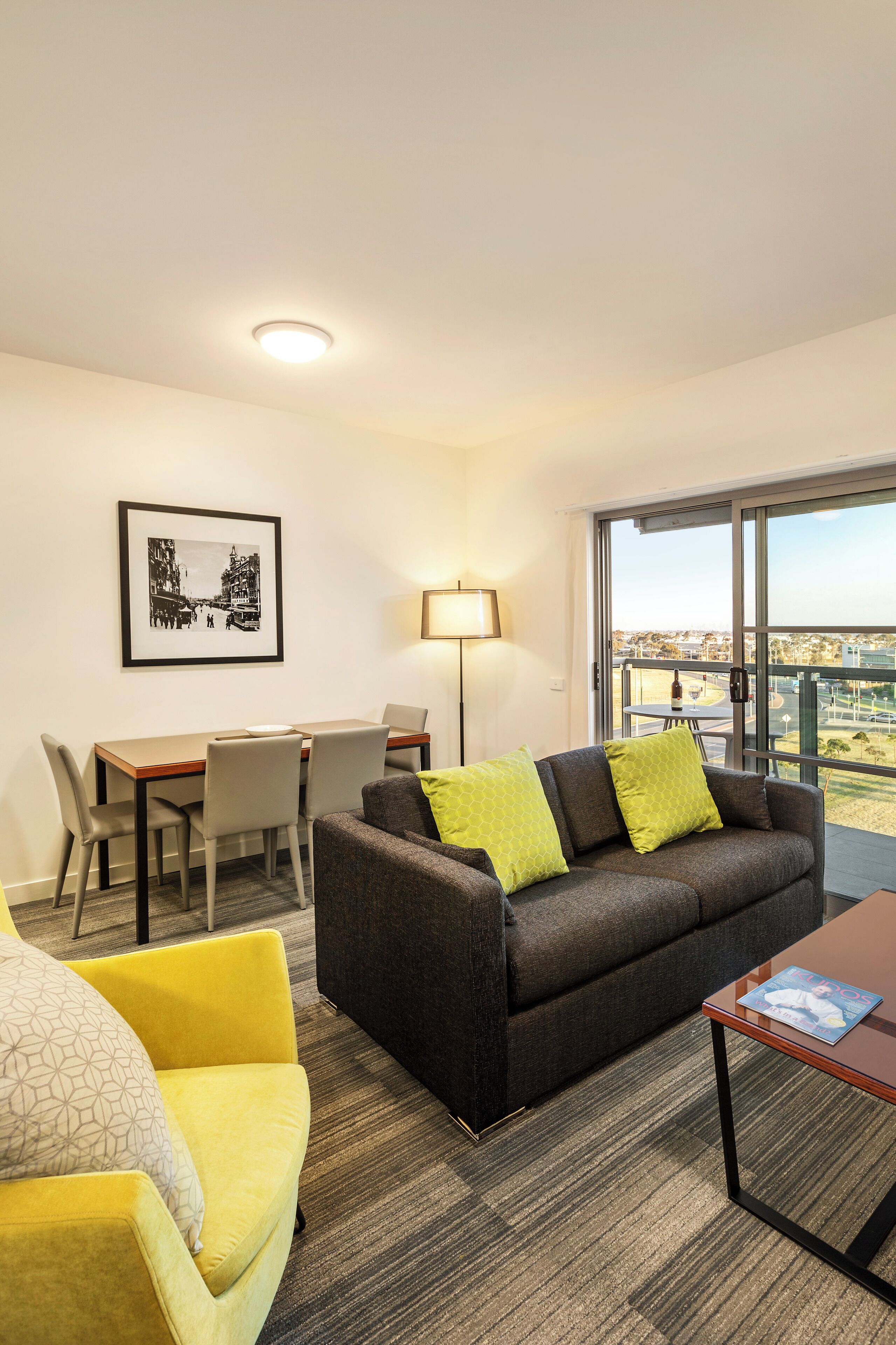 A modern hotel room with a balcony, a dining area, and a sofa with green cushions.