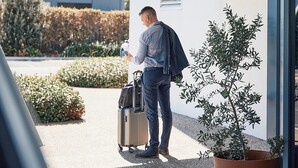 A man with a suitcase standing under a sign that reads "QUEST Melbourne Airport". - Quest Melbourne Airport (Melbourne Airport)