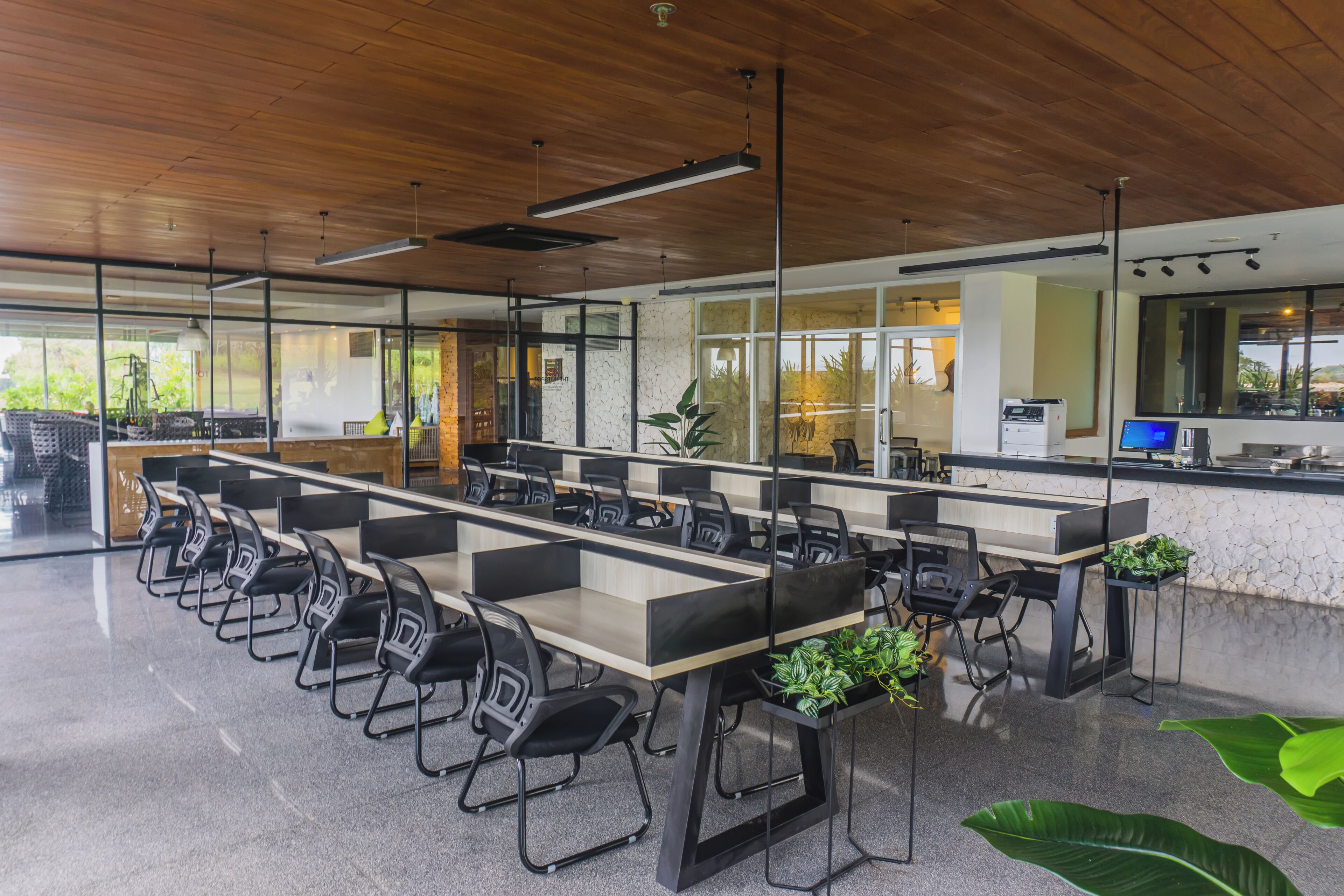 A modern office space with long tables, black chairs, and potted plants.