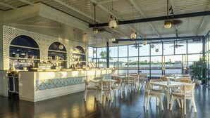 A spacious restaurant with a bar area, large windows, and a view of the water. - Klapa Resort (Pecatu)