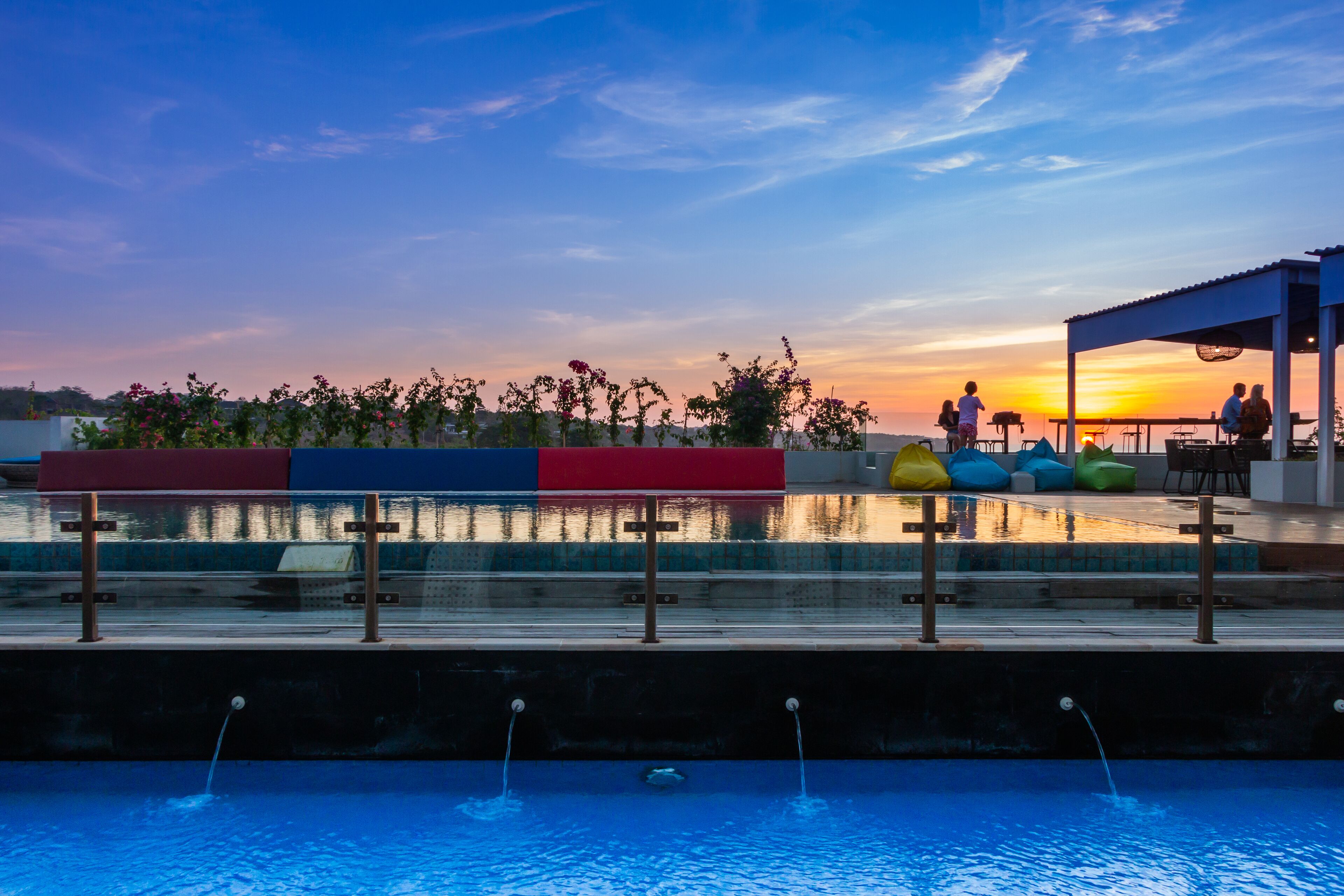 Zona de piscina con vista al atardecer, área de estar cubierta y fuente de agua.